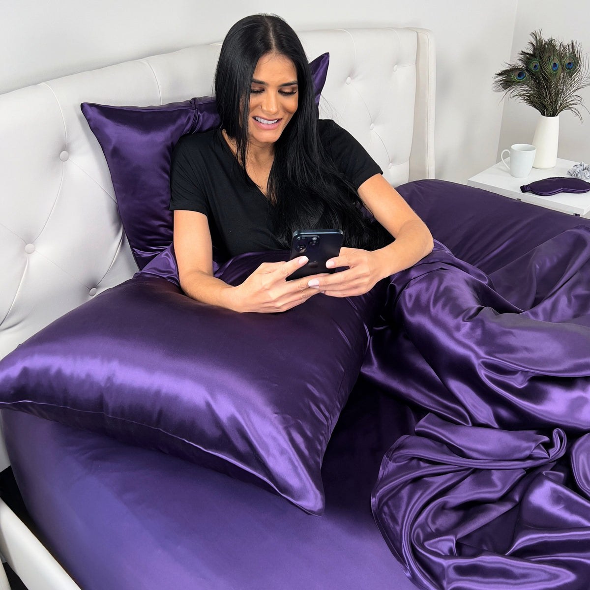 Woman resting in bed, using phone with 22 Momme silk Plum luxury pillow for back support