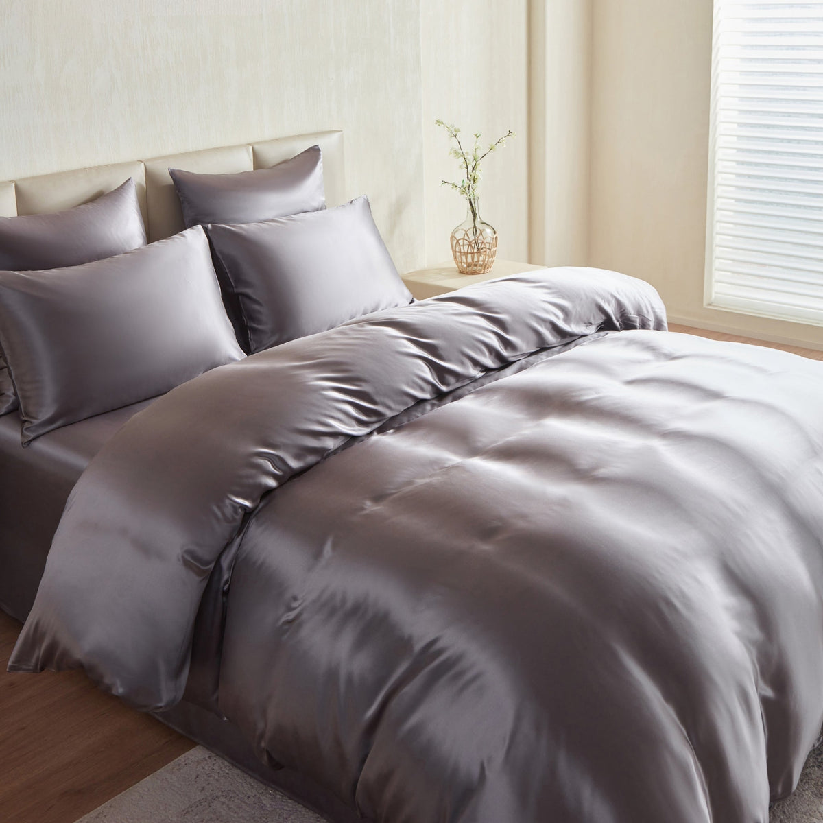 Gray silk comforter set on a bed in a bedroom with light decor.