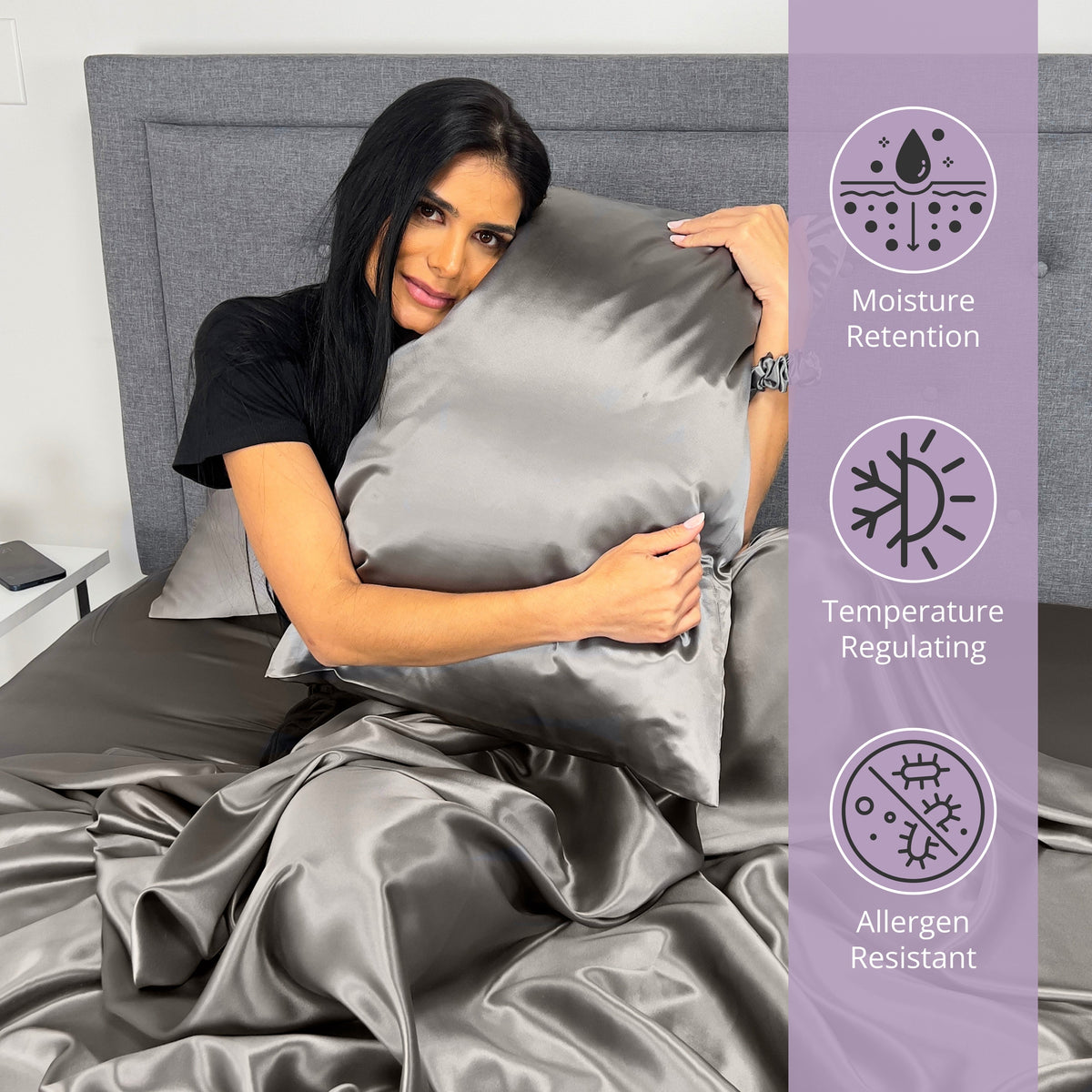 Woman sitting on bed, holding a gunmetal silk pillow and enjoying the comfort of silk sheets