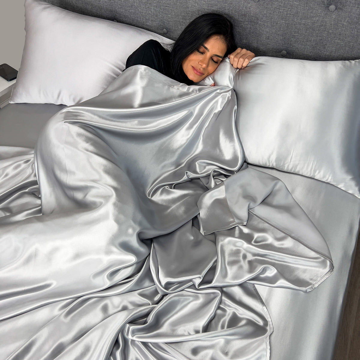 Woman wrapped in a silky silver sheet, lying comfortably on a plush bed
