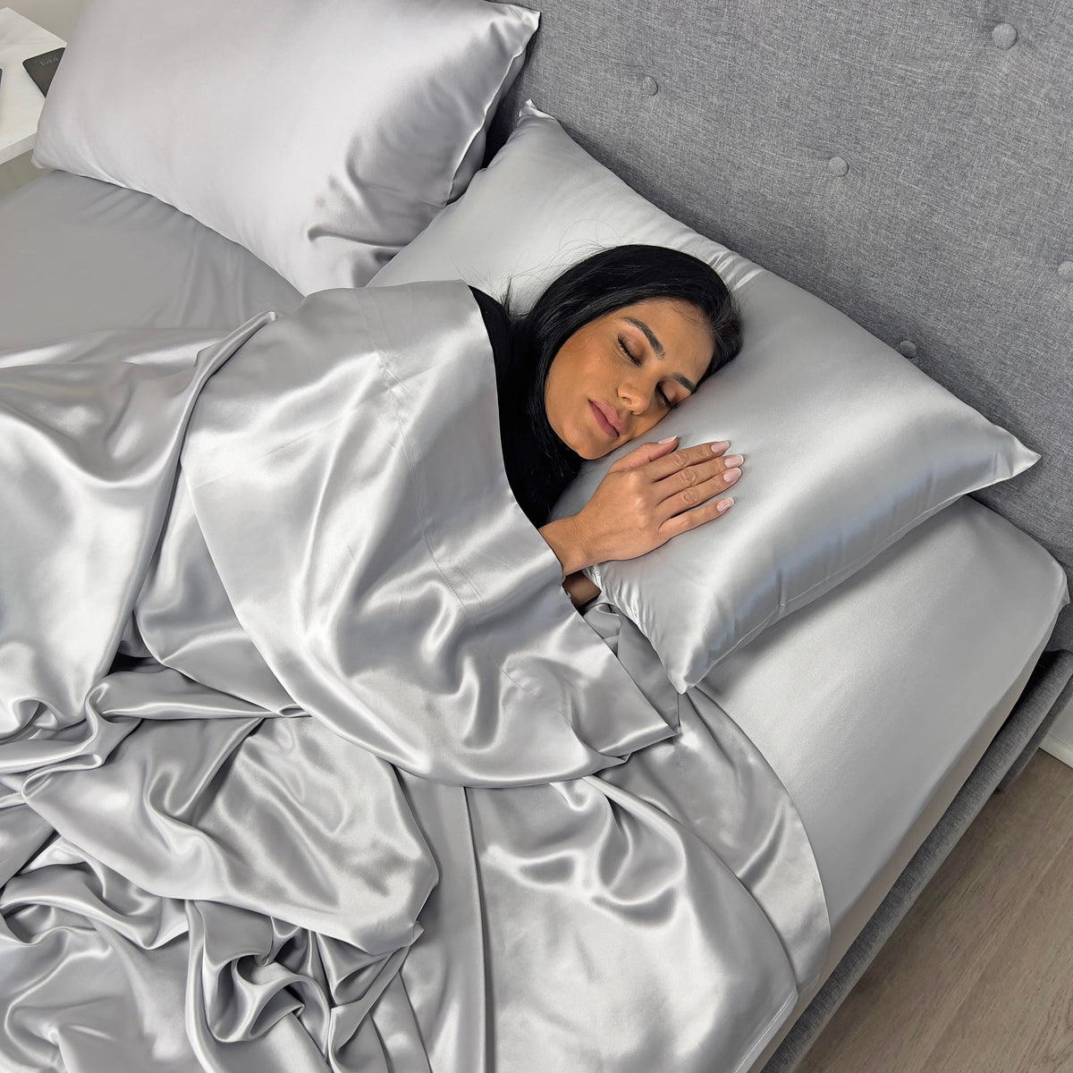 Woman sleeping on silver silk sheets, showcasing silk’s hydrating benefits for skin and hair