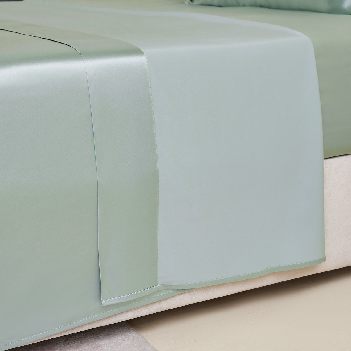 Close-up of a sage silk sheet on a bed, highlighting its delicate stitching and sheen