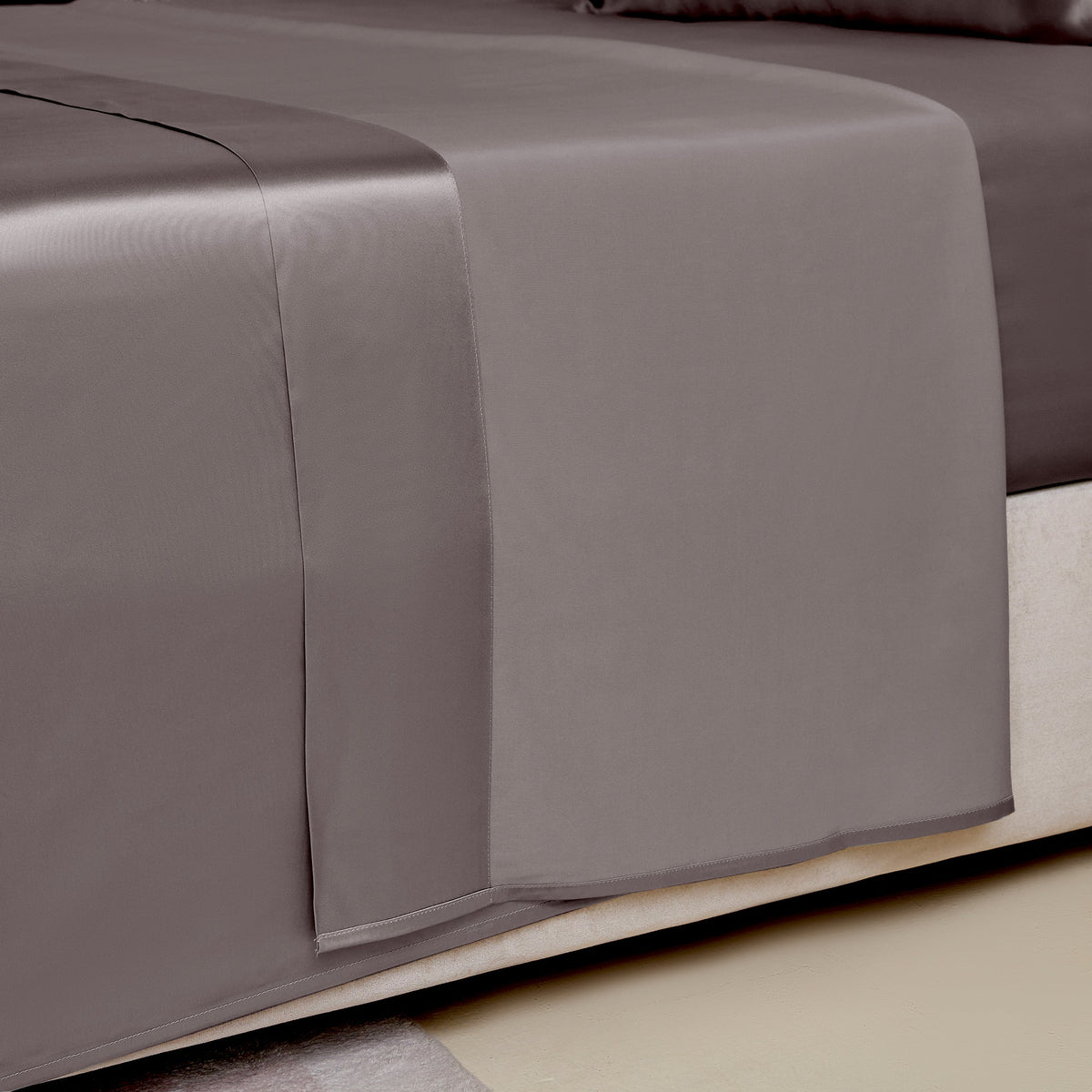 Close-up of a gunmetal silk sheet on a bed, highlighting its delicate stitching and sheen