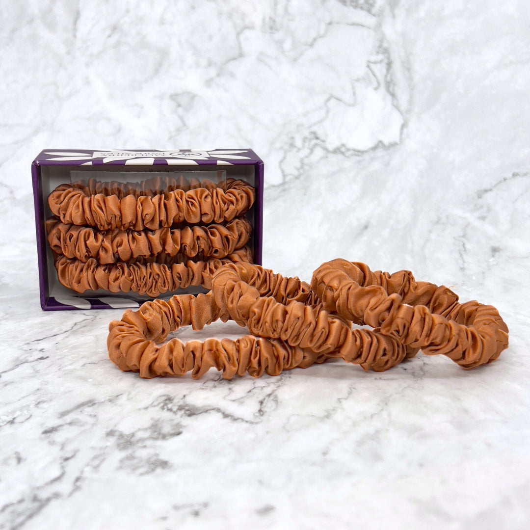 Silk Scrunchies - Copper from Mulberry Park Silks, featuring three brown elastic scrunchies made of 100% pure Mulberry Charmeuse silk, displayed on a marble surface.