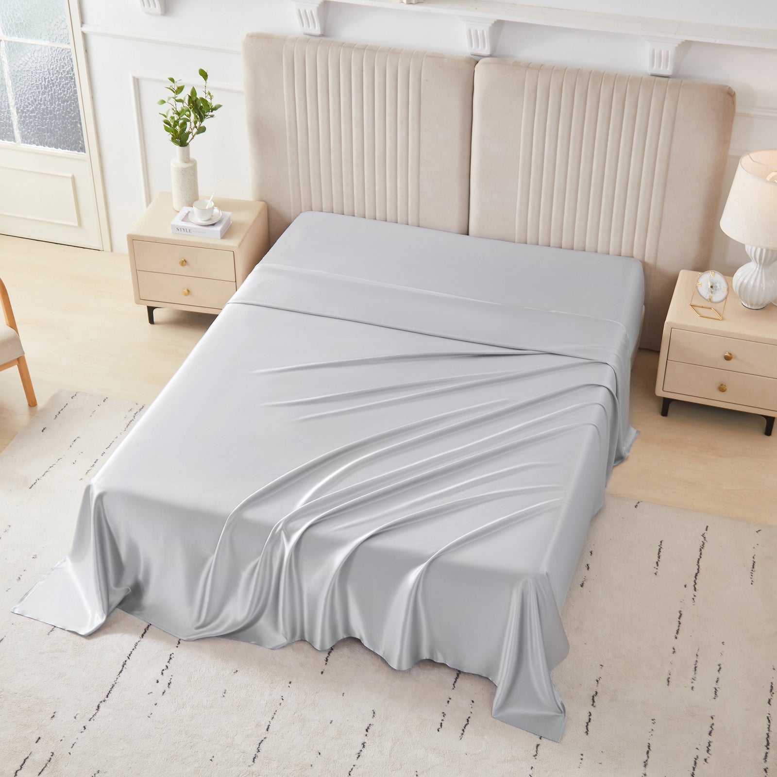 Silver silk flat sheet draped over a neatly made bed in a bright, modern bedroom