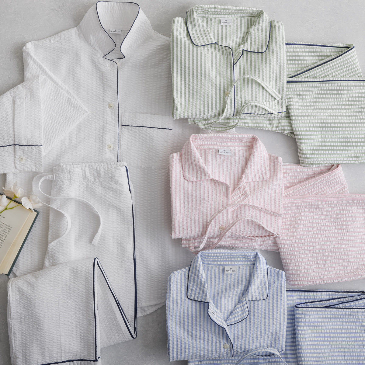 Five sets of seersucker cotton pajamas in white, green, pink, blue, and gray are neatly arranged on a flat surface.