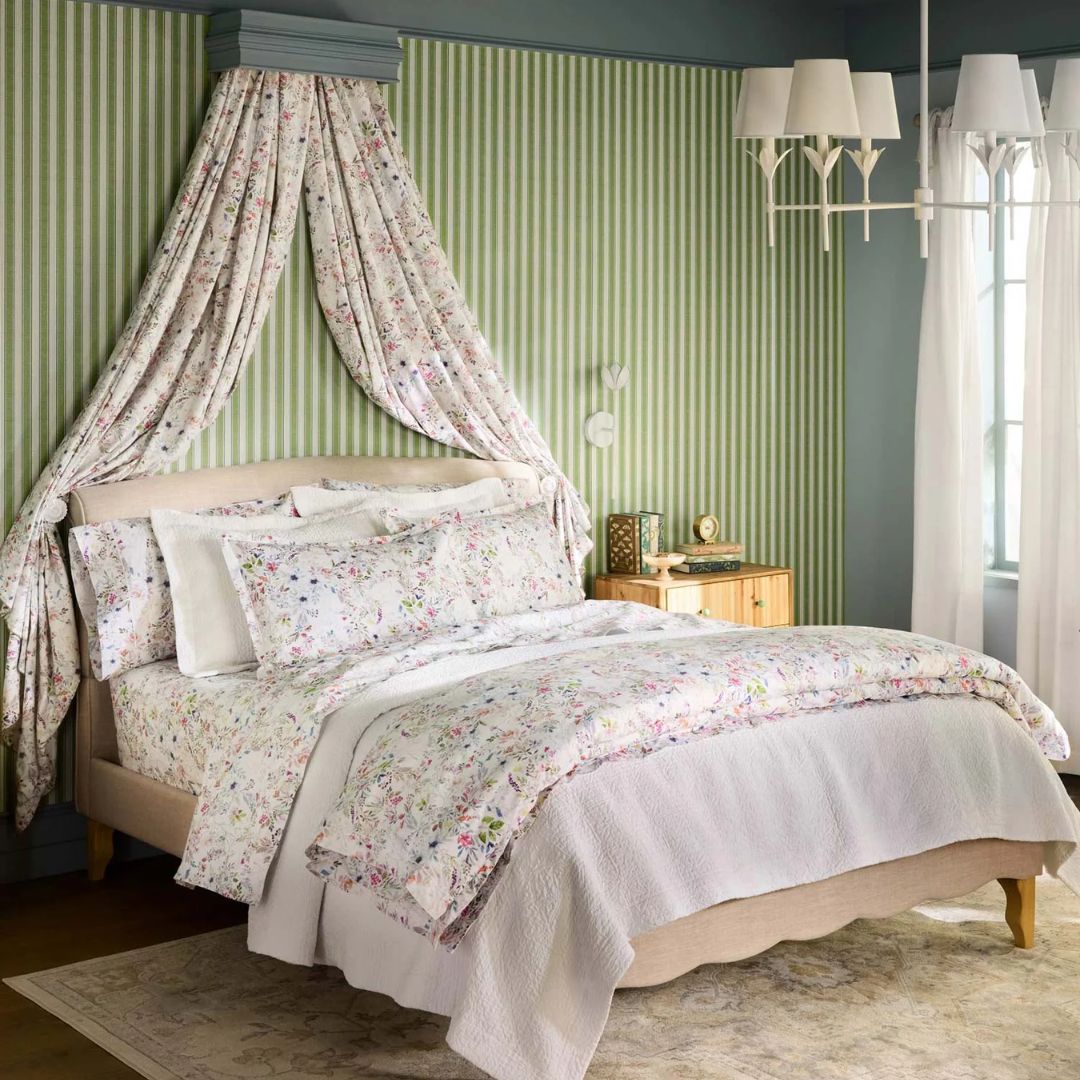 Floral bedding set on a bed with striped walls and a chandelier in a bedroom.