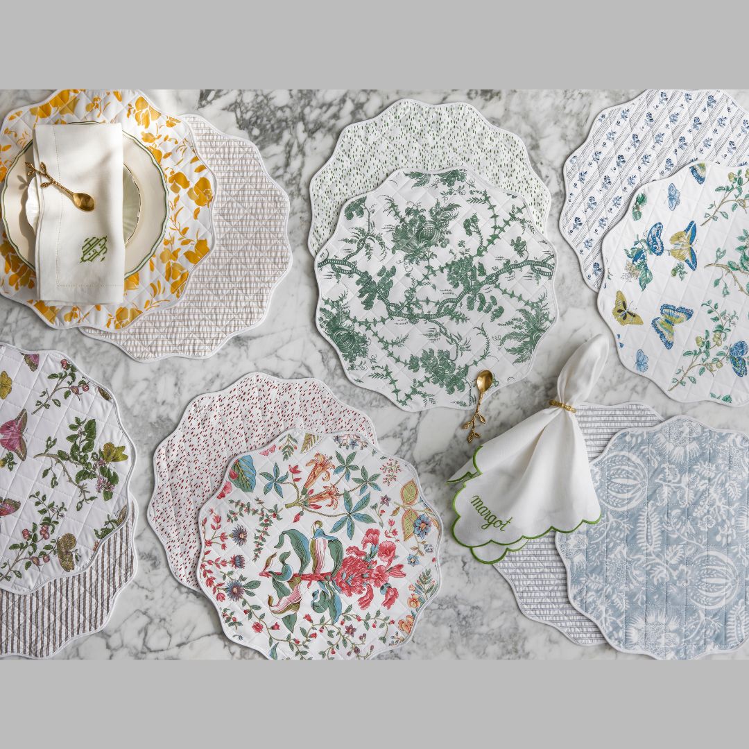 six different Matouk Reversible Placemats shown on top of a marble counter, with napkins and plates