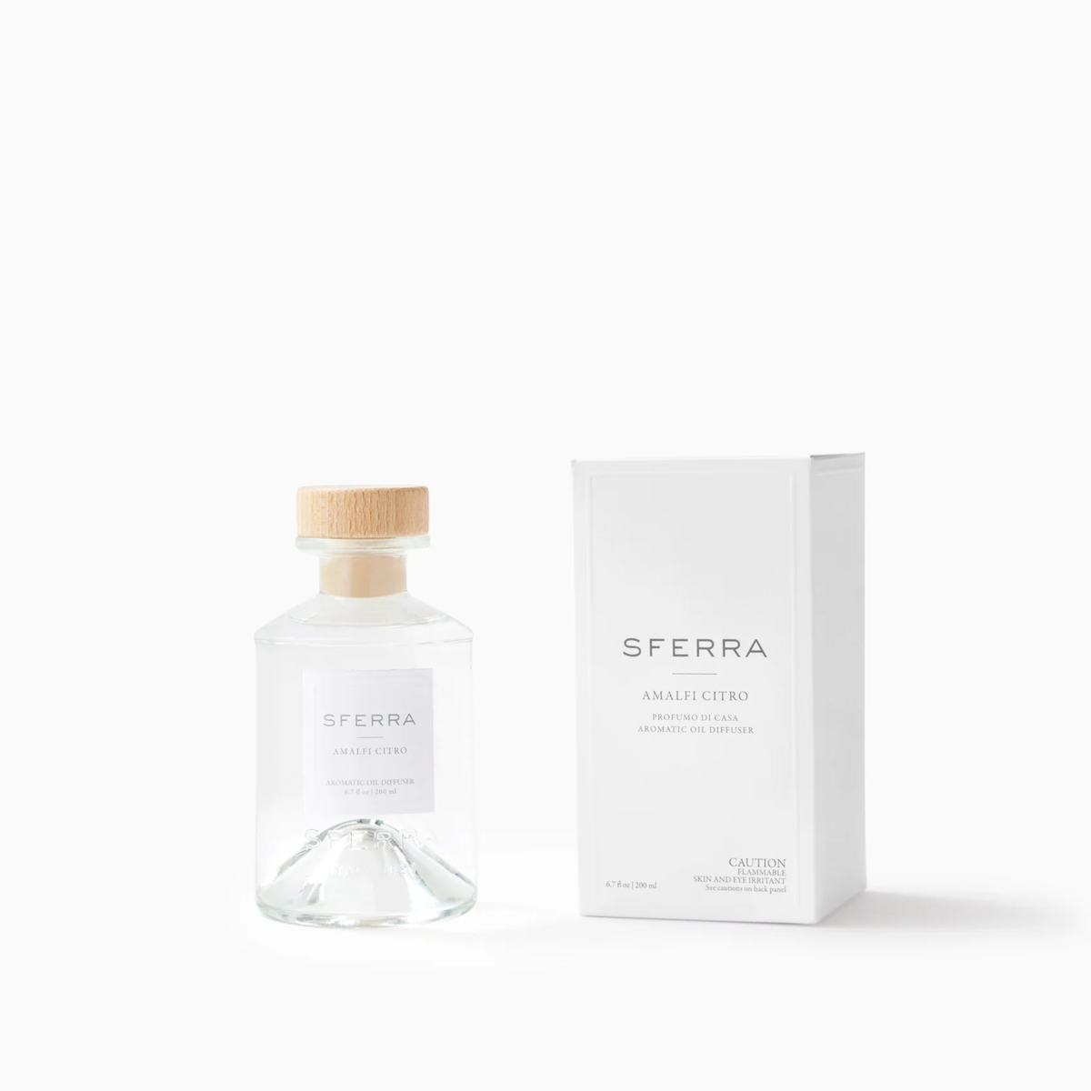 A clear glass bottle with a wooden cap by SFERRA home fragrance, featuring an Amalfi citrus scent, sits beside its box.