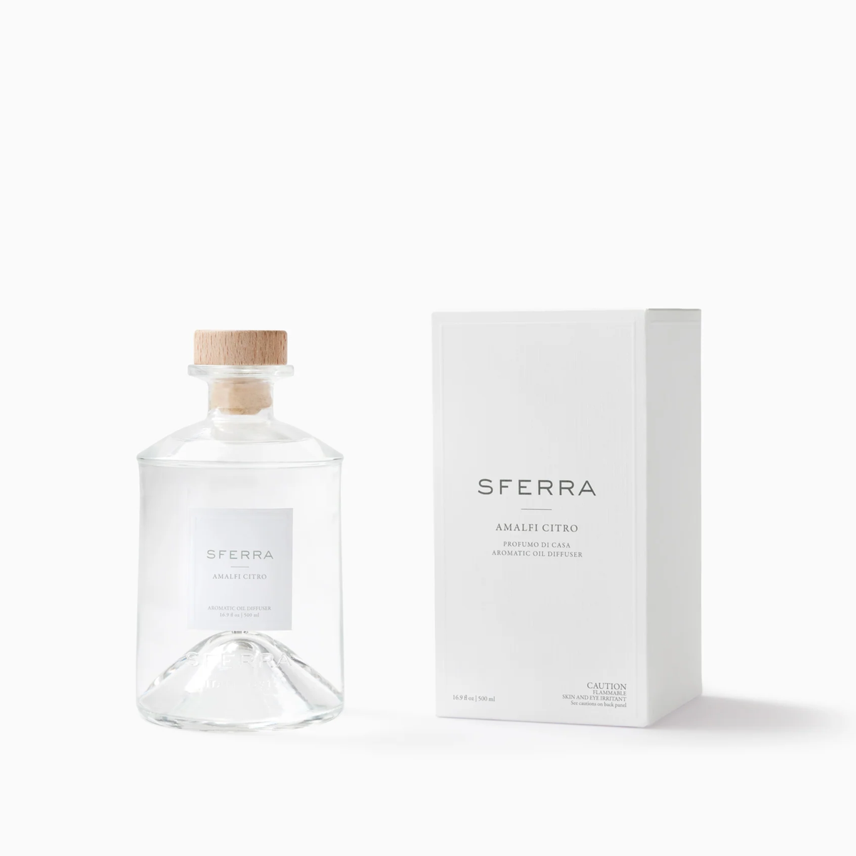 Clear glass bottle with wooden stopper, SFERRA home fragrance in an Amalfi citrus scent, beside its matching white box.