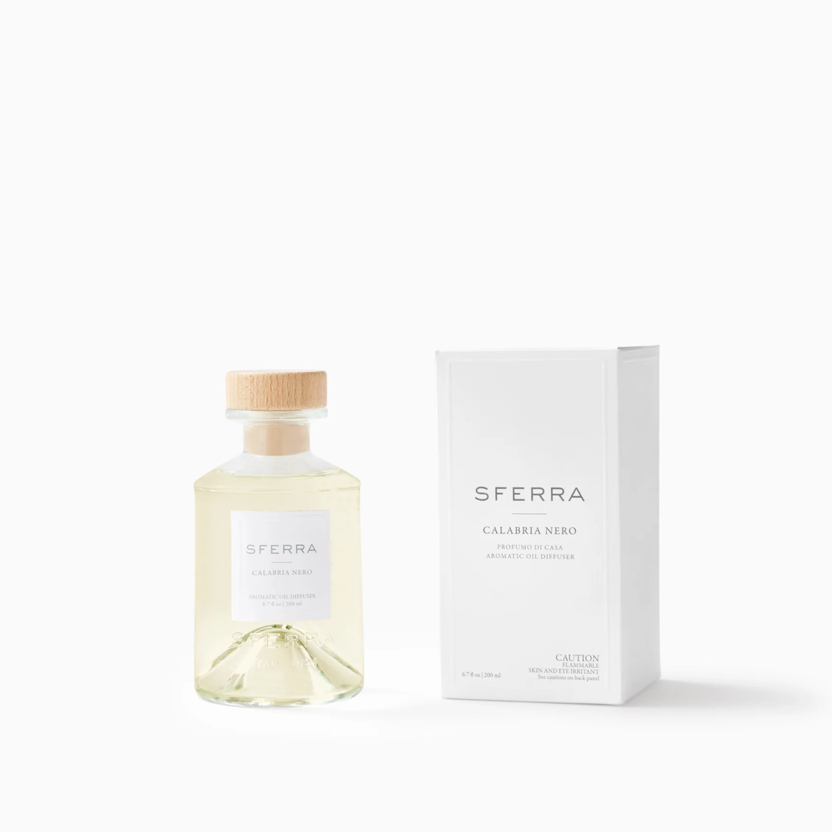 Clear bottle with light liquid and wooden cap beside a white SFERRA Profumo di Casa box— Calabria Nero scents, Italian-inspired.