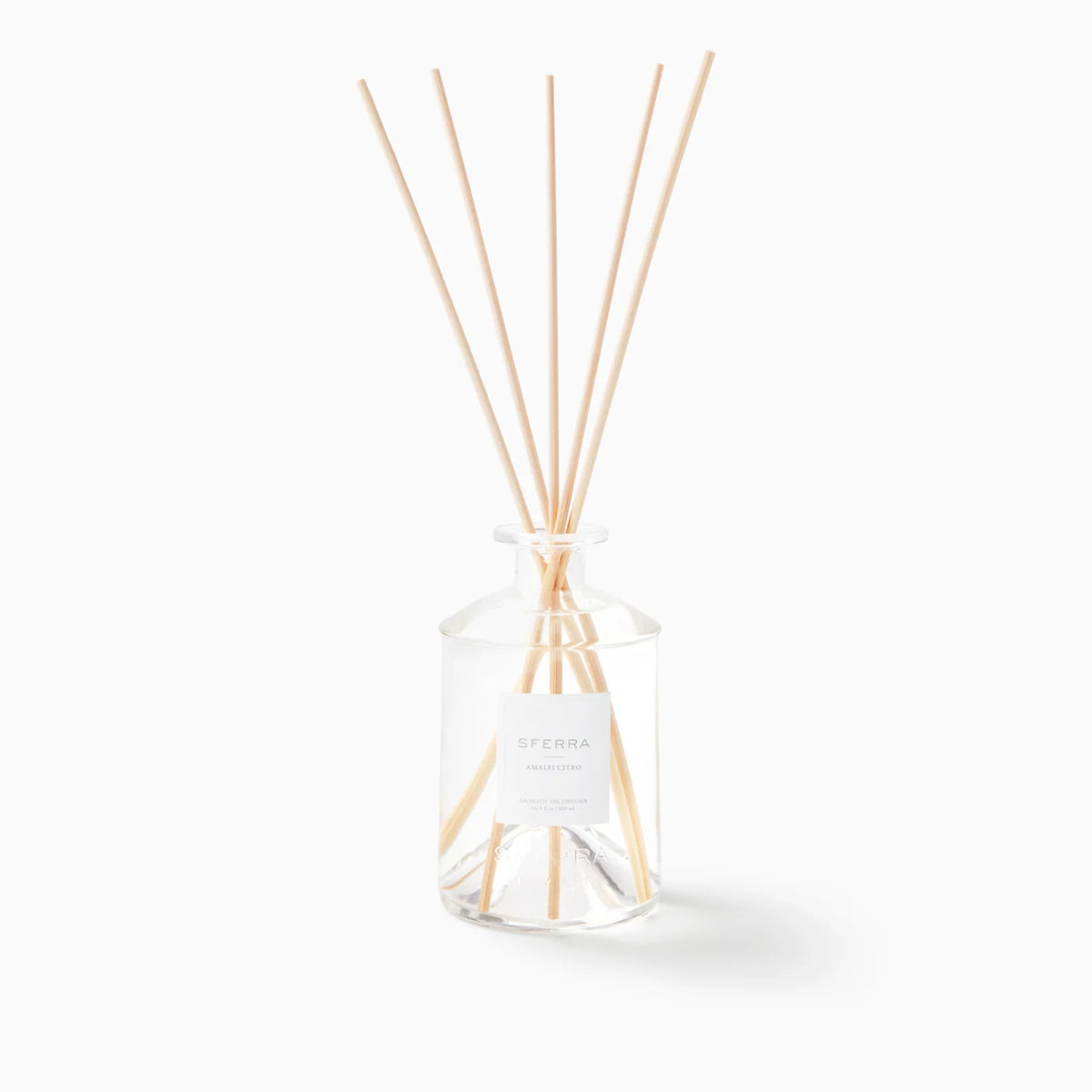 A clear glass SFERRA home fragrance diffuser with reeds, labeled Sferra, evokes an Italian-inspired home ambiance.