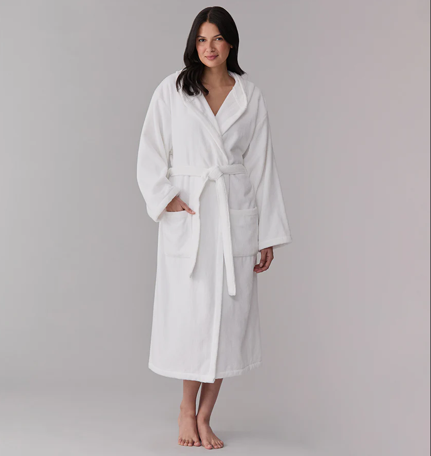 A woman stands barefoot in a luxury cotton robe, featuring front pockets and a waist tie, against a plain background.
