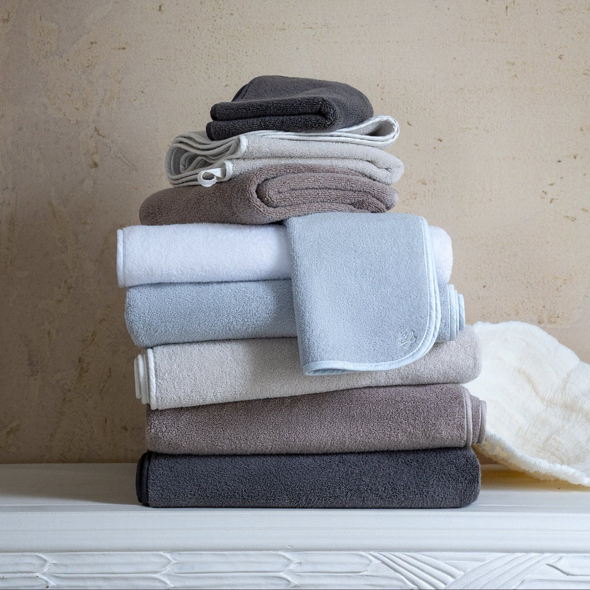 A stack of Scandia Home Delfine Bath Towels made from long-staple cotton sits on a white surface against a textured beige wall
