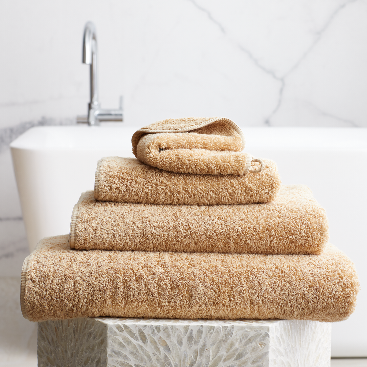 Stack of Bronze Scandia Home Indulgence Towels on a bathroom counter with a blurred tub in background