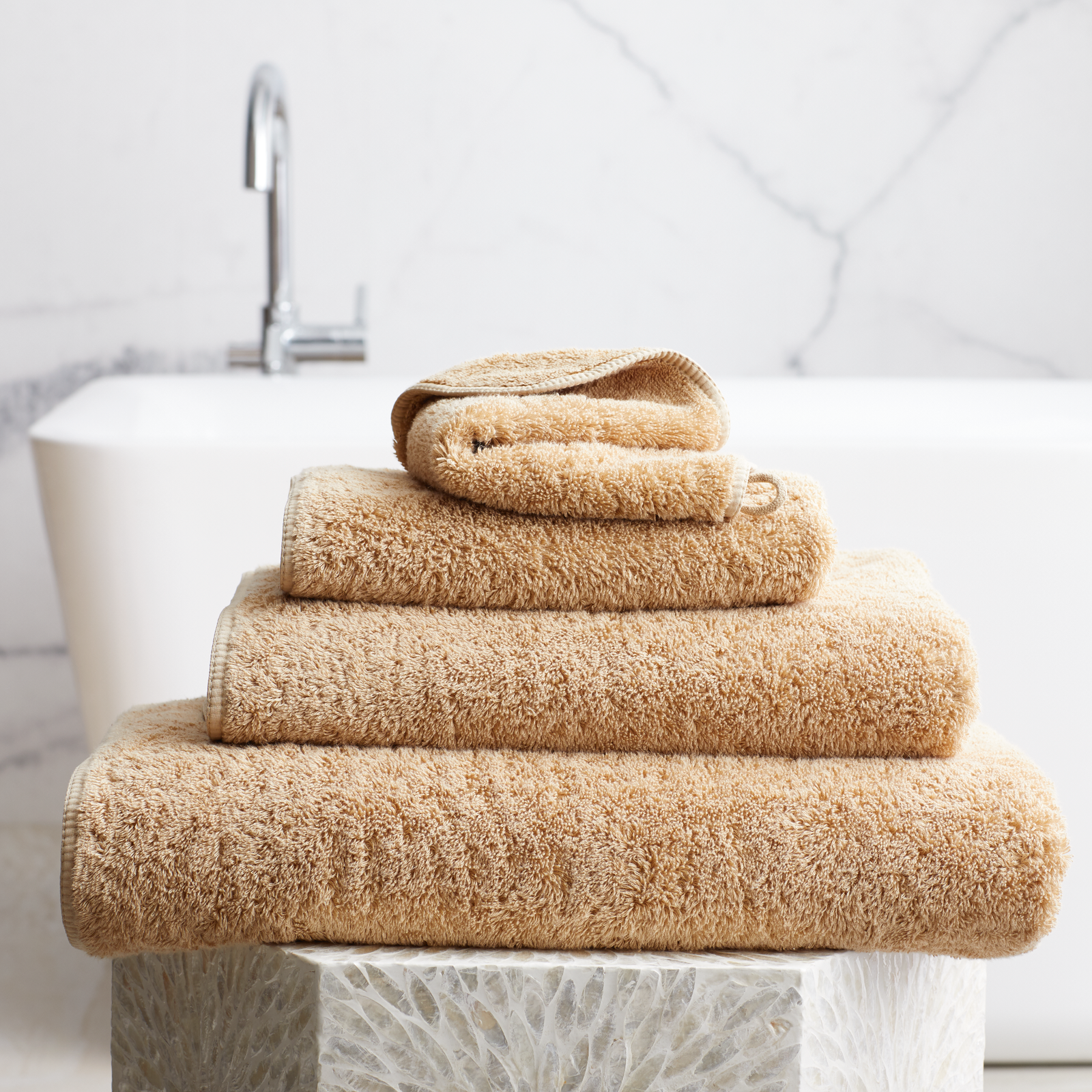 Stack of Bronze Scandia Home Indulgence Towels on a bathroom counter with a blurred tub in background