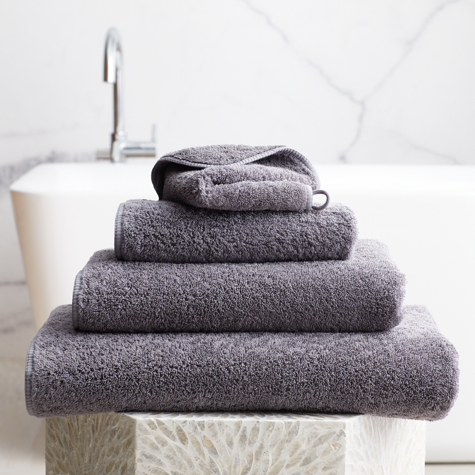 Stack of Charcoal Scandia Home Indulgence Towels on a bathroom counter with a blurred tub in background