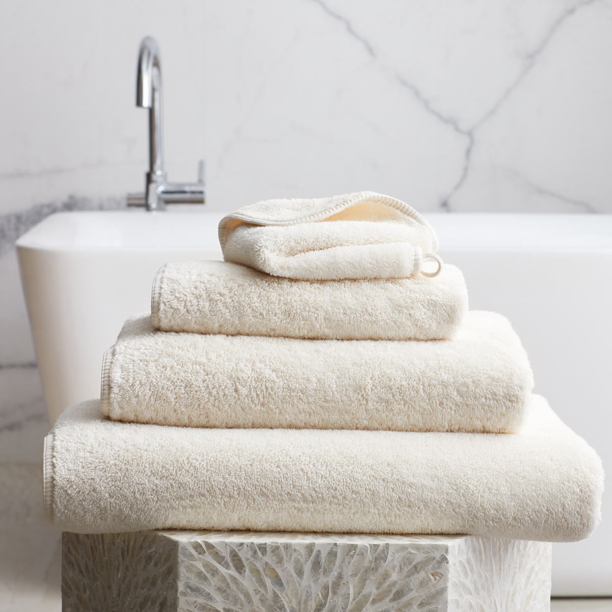 Stack of Ivory Scandia Home Indulgence Towels on a bathroom counter with a blurred tub in background