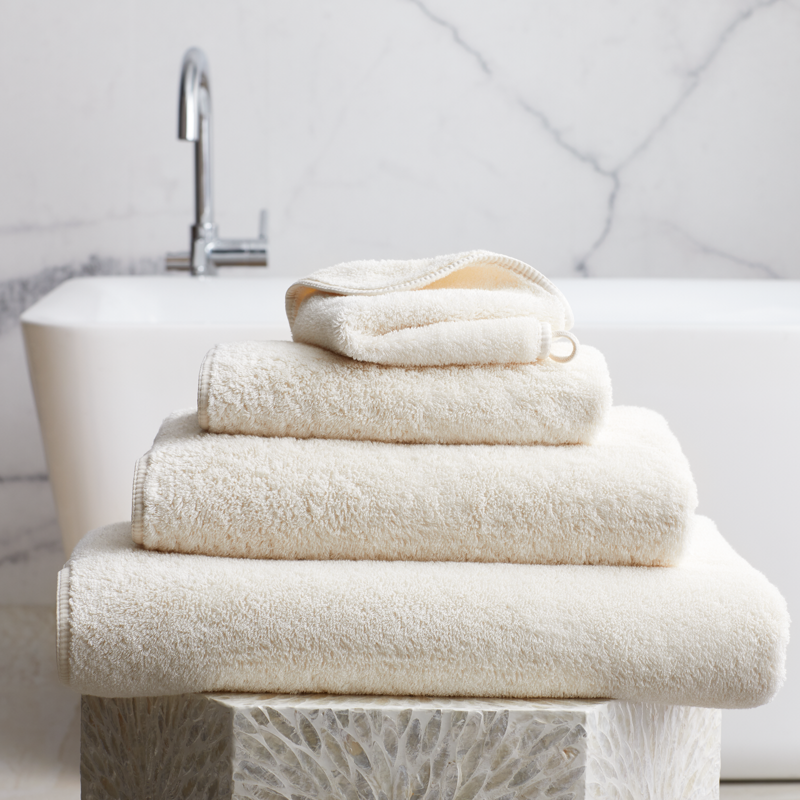 Stack of Ivory Scandia Home Indulgence Towels on a bathroom counter with a blurred tub in background
