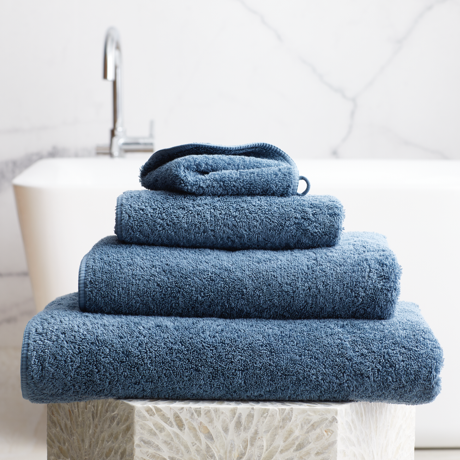 Stack of Petrol Scandia Home Indulgence Towels on a bathroom counter with a blurred tub in background