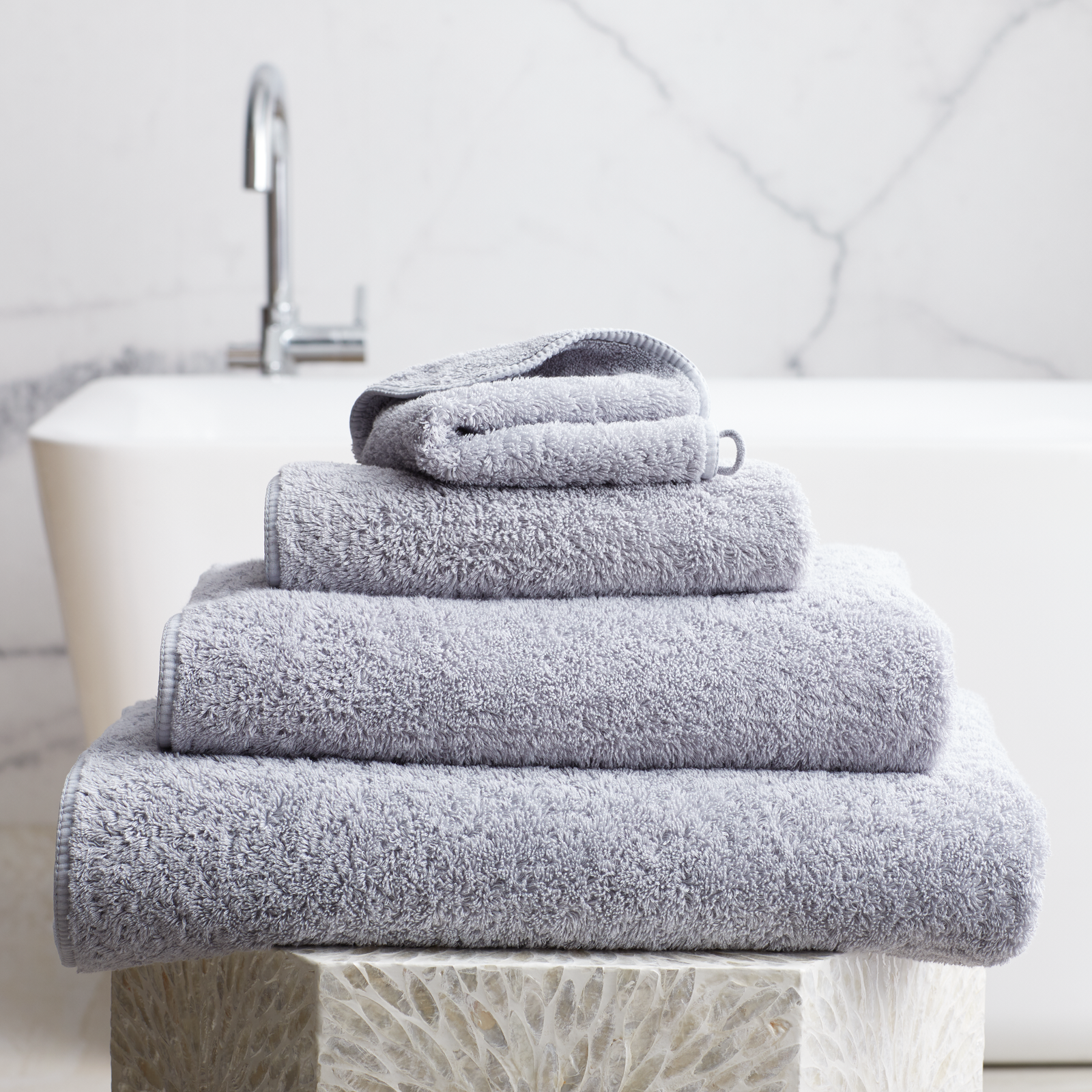 Stack of Silver Scandia Home Indulgence Towels on a bathroom counter with a blurred tub in background