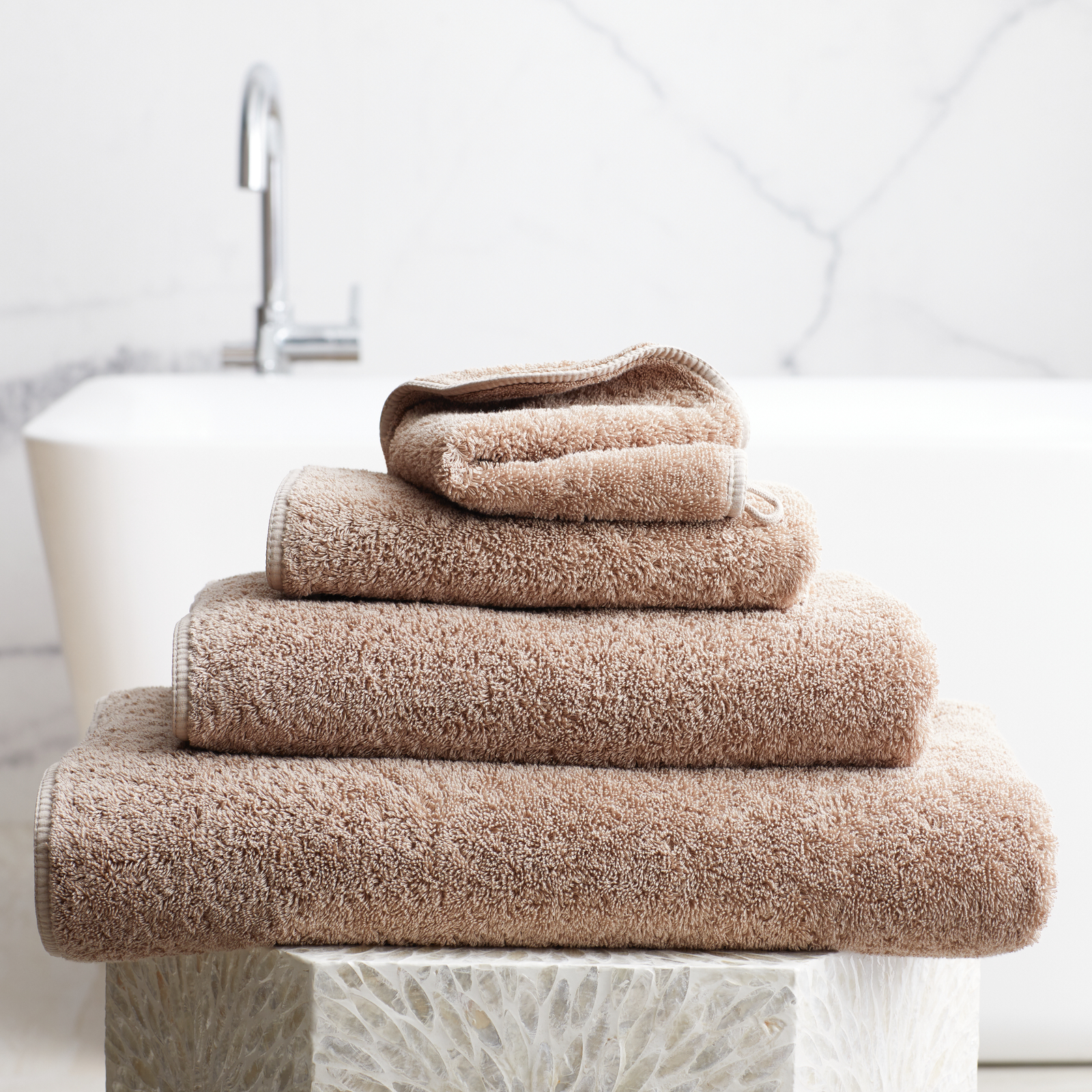 Stack of Truffle Scandia Home Indulgence Towels on a bathroom counter with a blurred tub in background