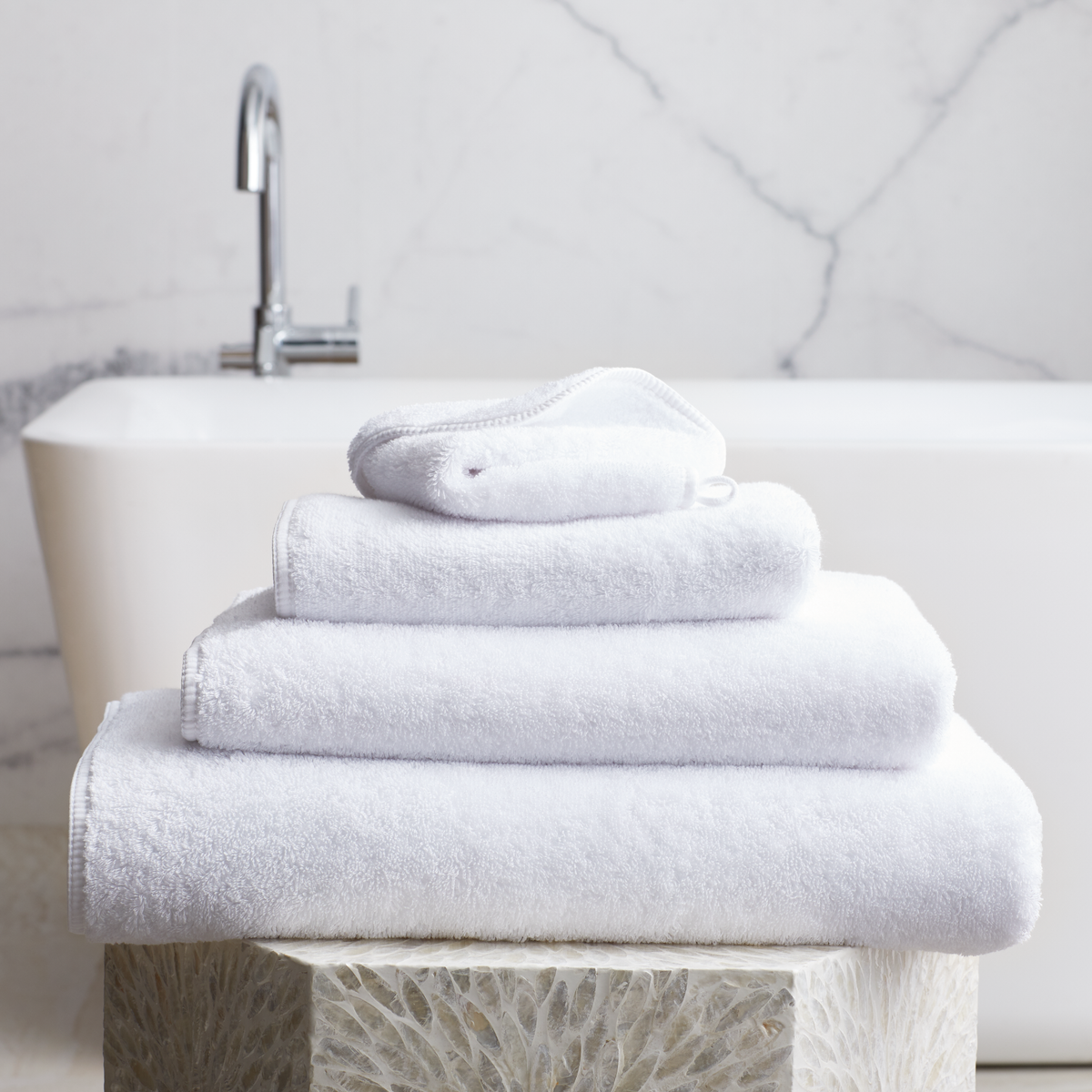 Stack of White Scandia Home Indulgence Towels on a bathroom counter with a blurred tub in background