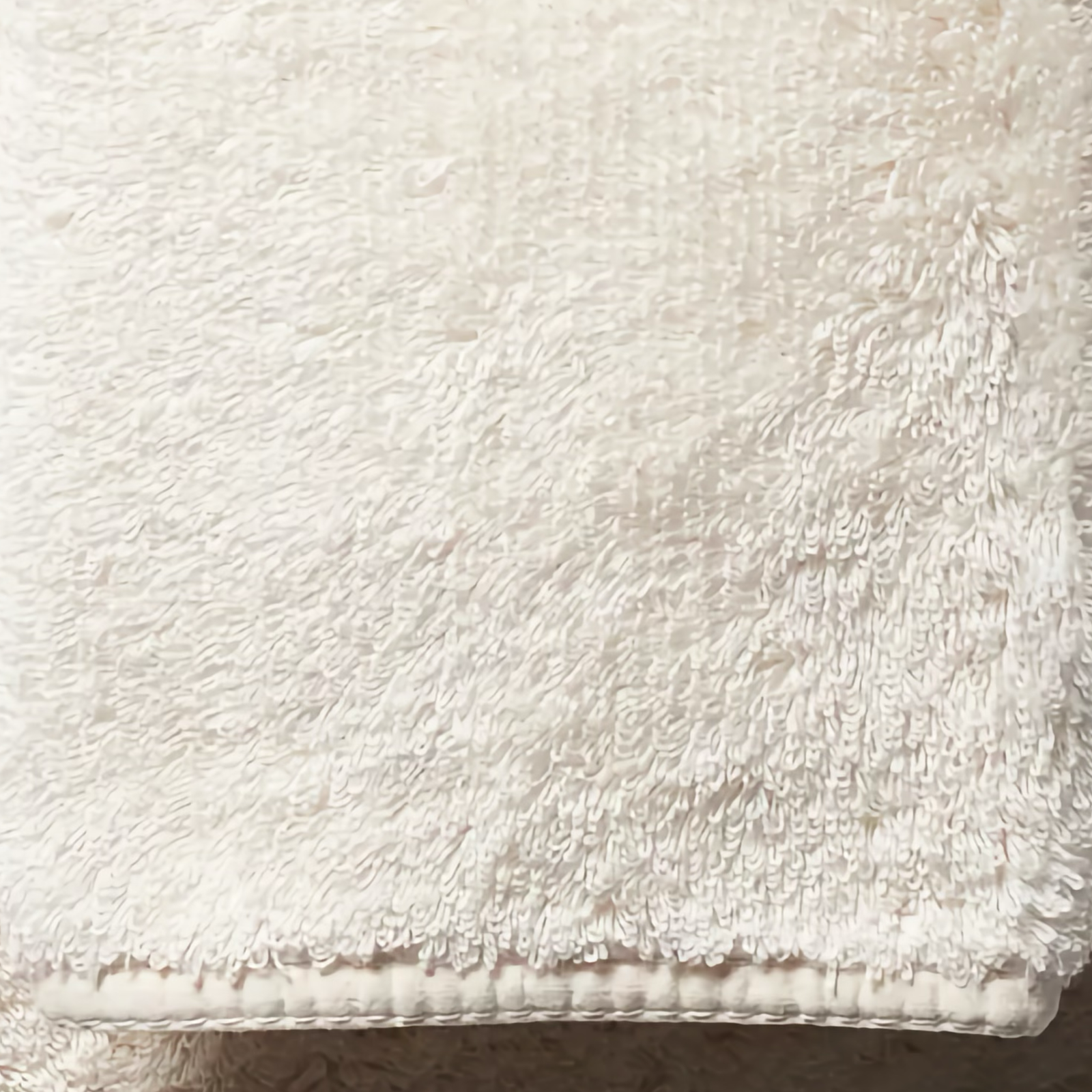 Stack of Ivory Scandia Home Indulgence Towels on a bathroom counter with a blurred tub in background