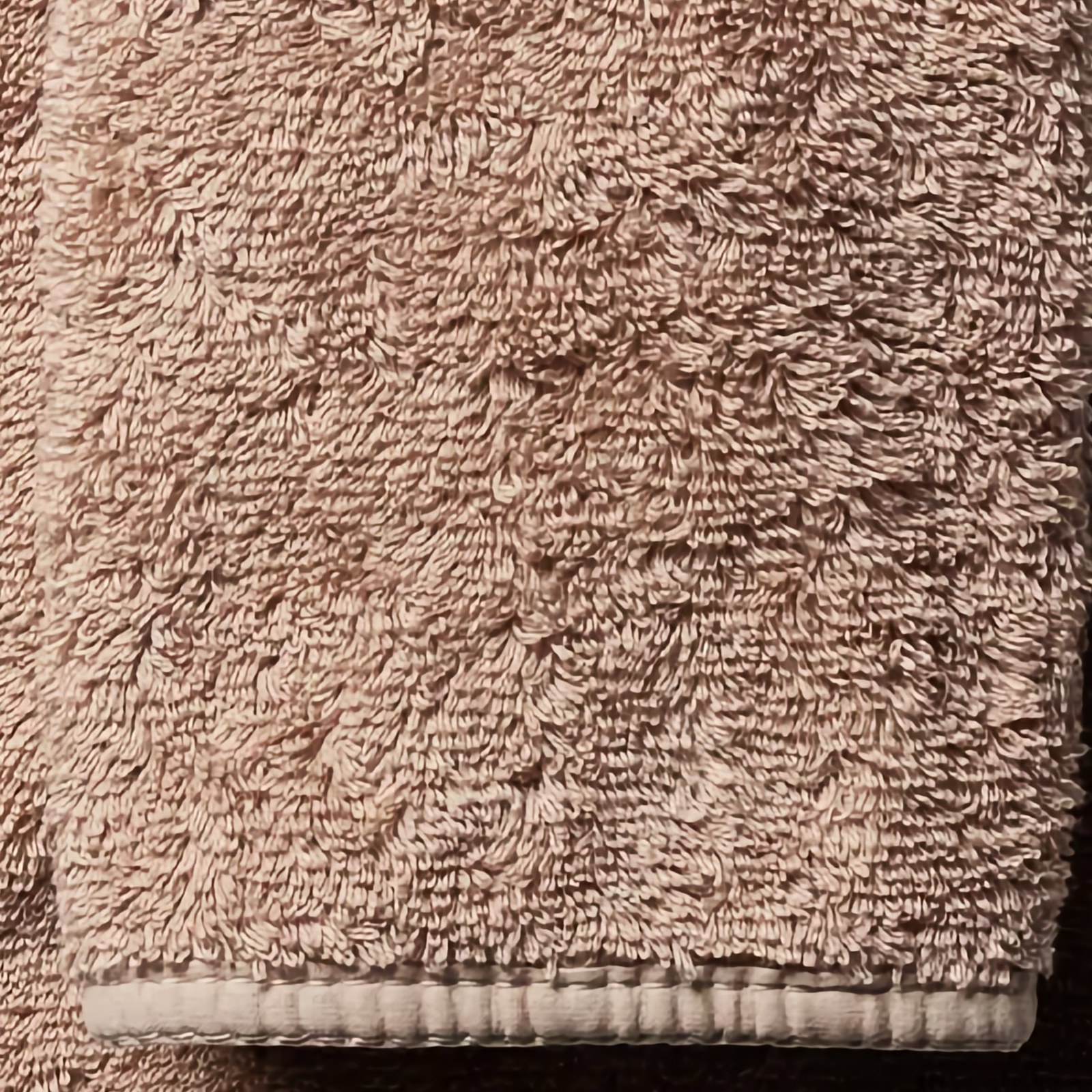 Stack of Truffle Scandia Home Indulgence Towels on a bathroom counter with a blurred tub in background