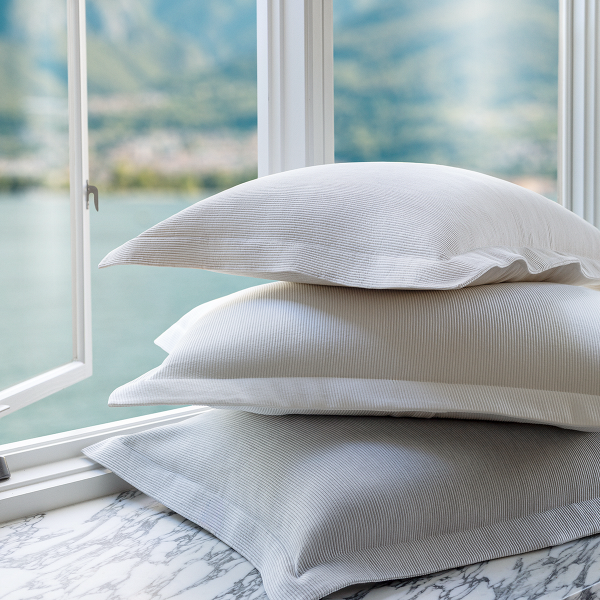 Stack of Scandia Home Lorenzo Pique Shams on a marble surface with a window view of mountains.