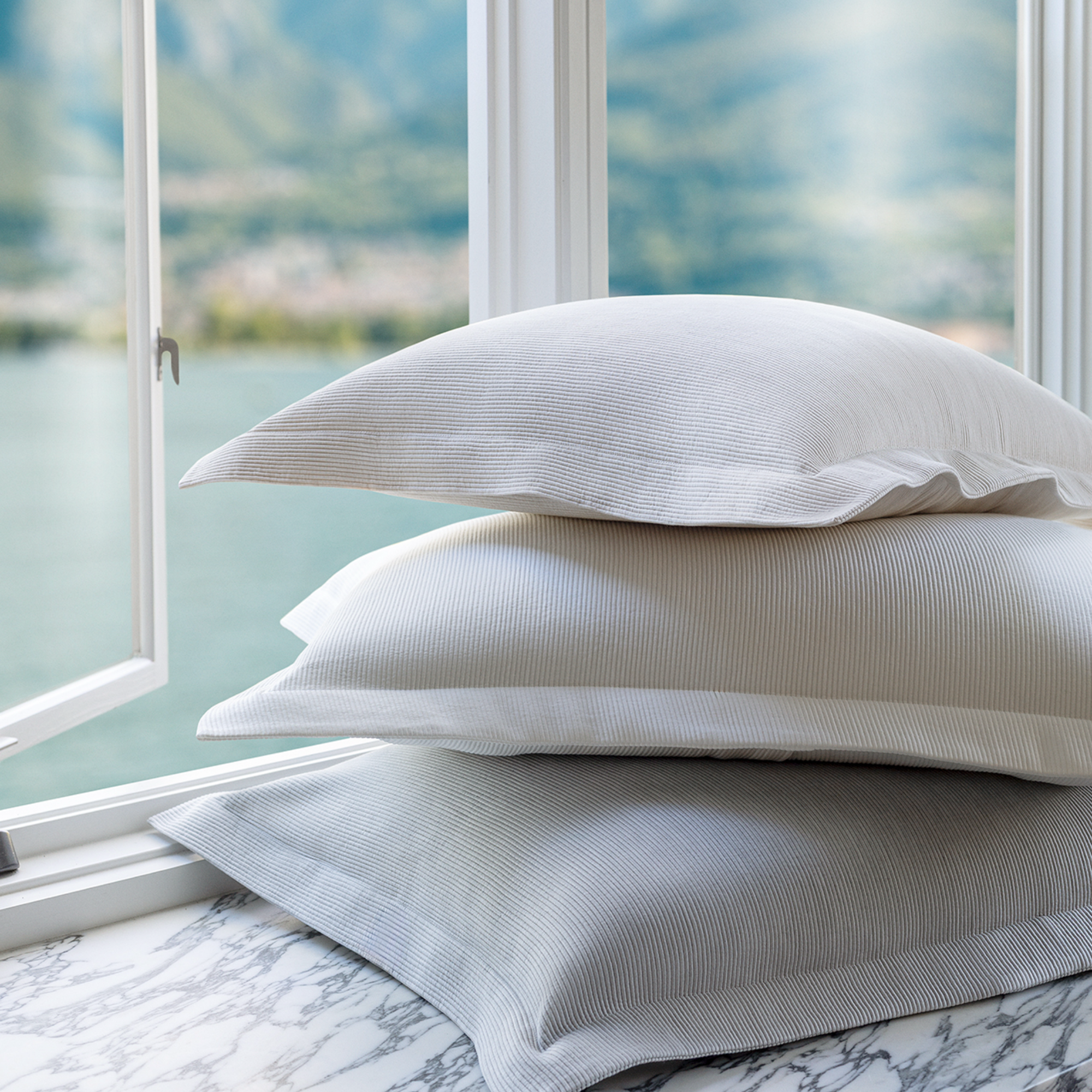 Stack of Scandia Home Lorenzo Pique Shams on a marble surface with a window view of mountains.