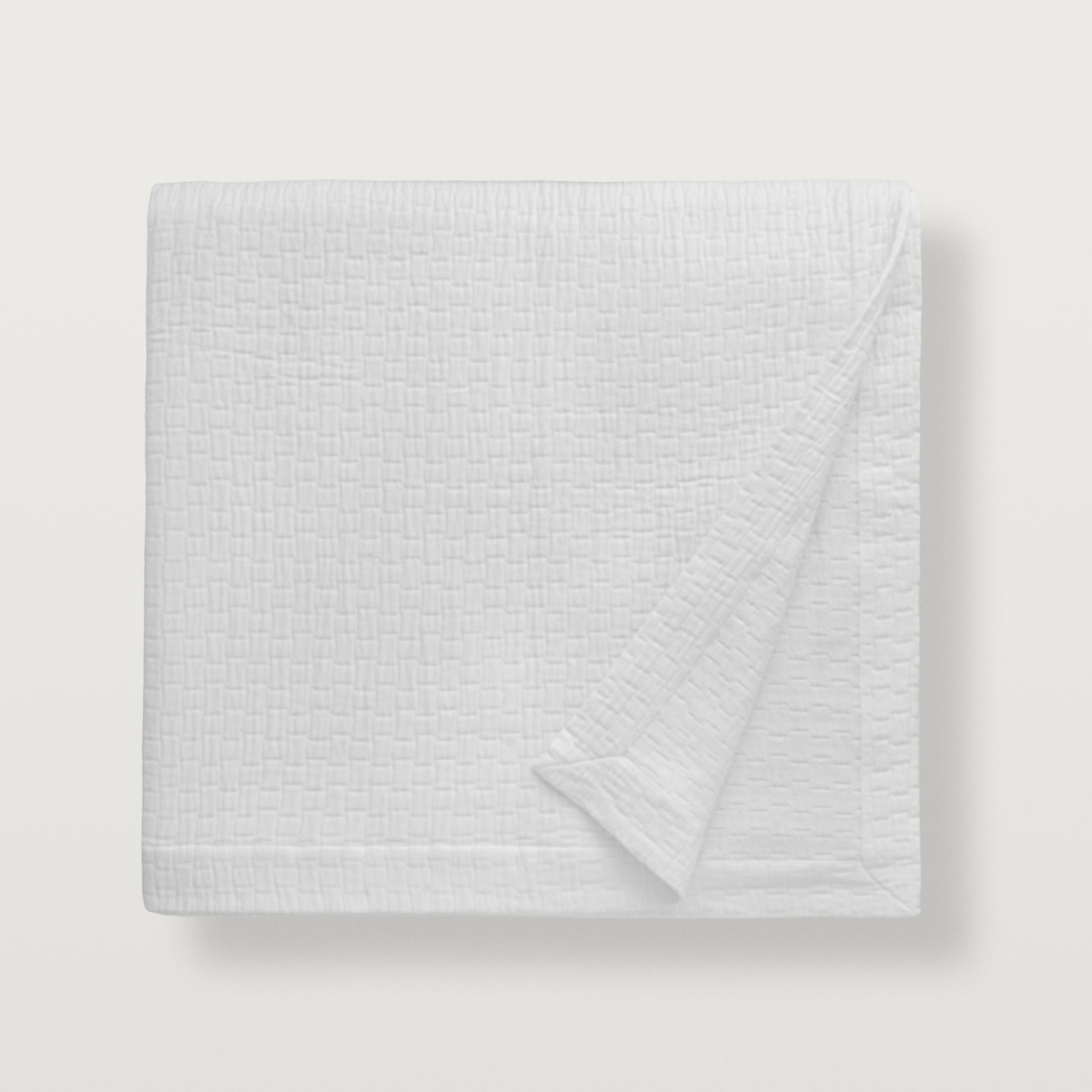 White Scandia Home Portia Matelasse Coverlet is neatly folded, one corner turned over on a white background