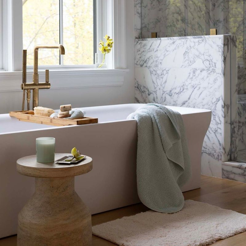 Modern bathroom with a bathtub, wooden stool, and decorative items. draped over the tub is the Scandia Home Indulgence towel in Ice