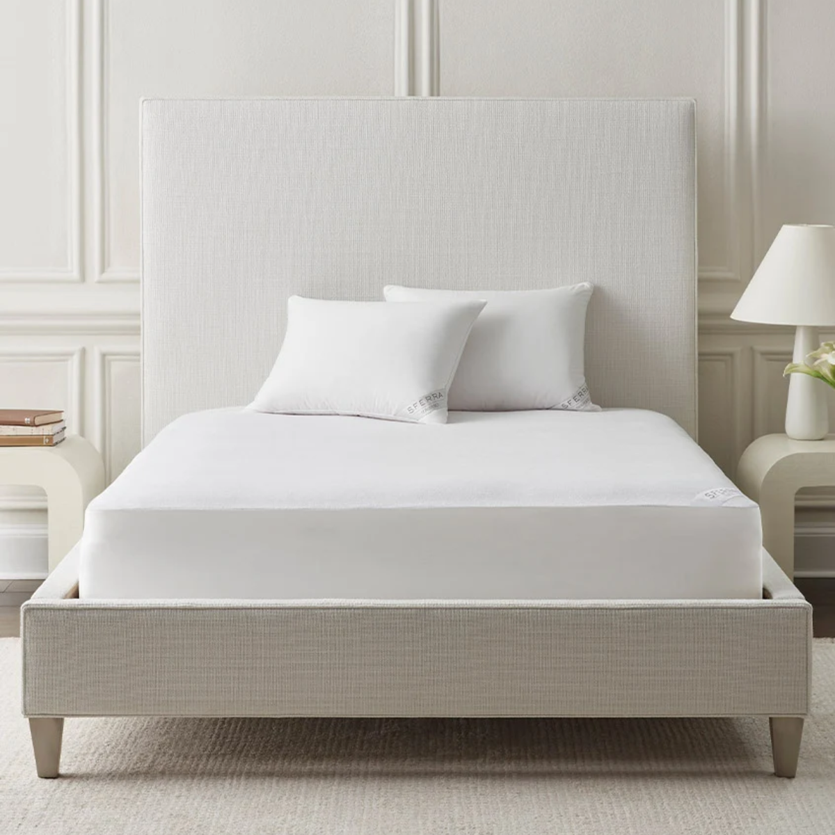 A neatly made bed two pillows, and a cotton terry Sferra Bailey Mattress Protector in a minimalist bedroom.
