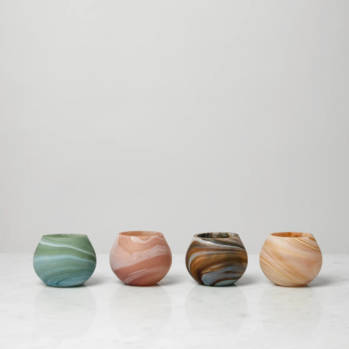 Four round, Sferra Giove Marbled Votive Holders in Bark, Almond, Paprika, and Clover designs