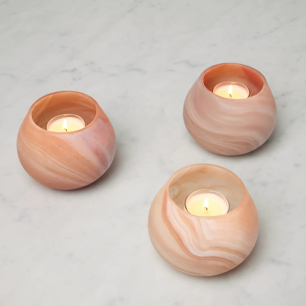 Three lit Paprika Sferra Giove Marbled Votive Holders add unique home decor charm to a white marble surface.