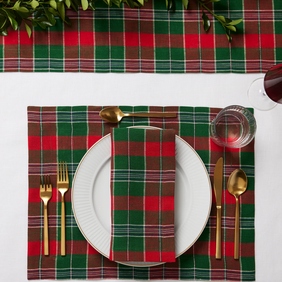 Table set with a white plate, gold cutlery, and Sferra Masseria Table Linens in Emerald and Red colors and a classic white tablecloth