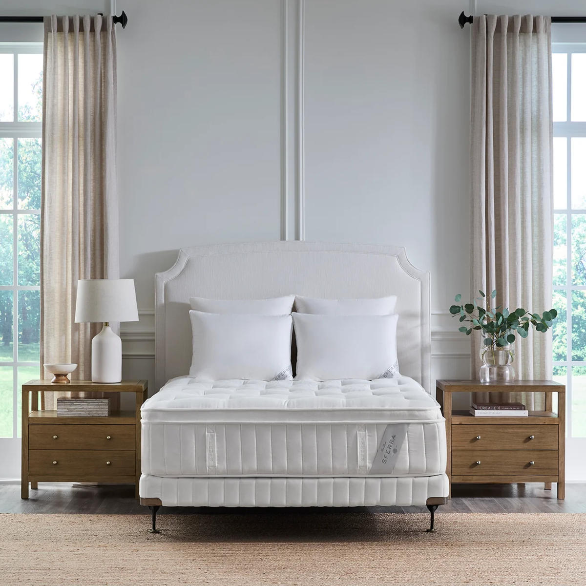 A neatly made bed with a luxury Sferra Nuvole CV Pillowtop Mattress, nightstands, lamps, and curtains in a bright, modern bedroom.