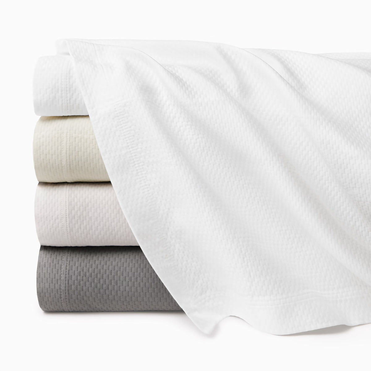 Four folded Sferra Perrio coverlets, made in Portugal from cotton matelassé, stacked in neutral tones.