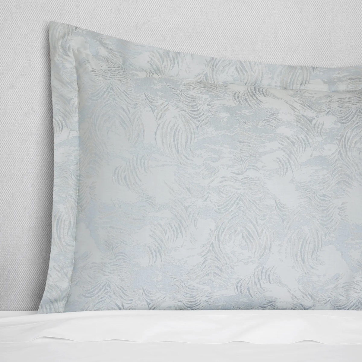 Light blue and white water-inspired jacquard pillow on a bed, paired with the Sferra Riflesso duvet cover.