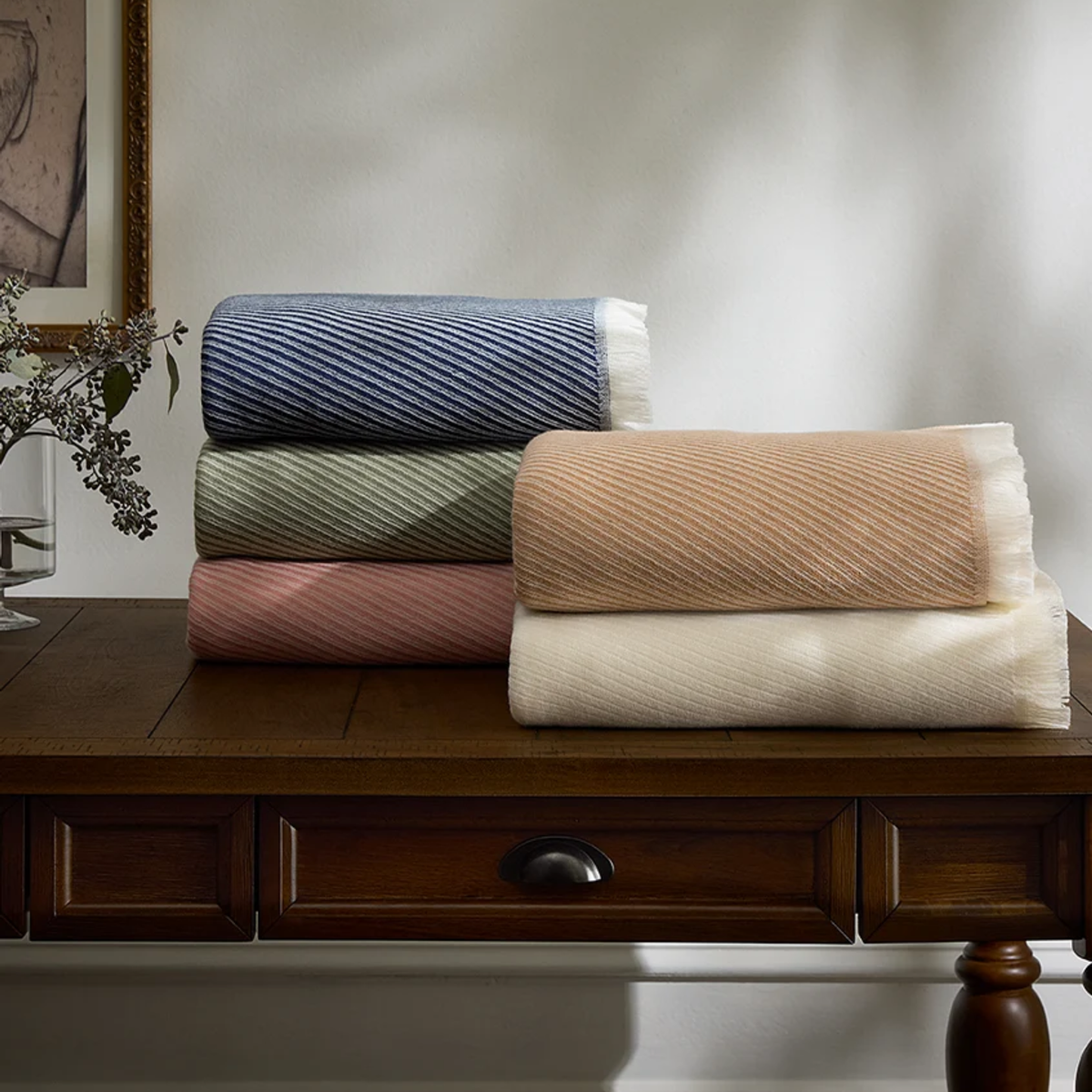 Sferra Taormina Throws in Ecru, Sand, Sage, Rose and Baby colors folded on a drawer