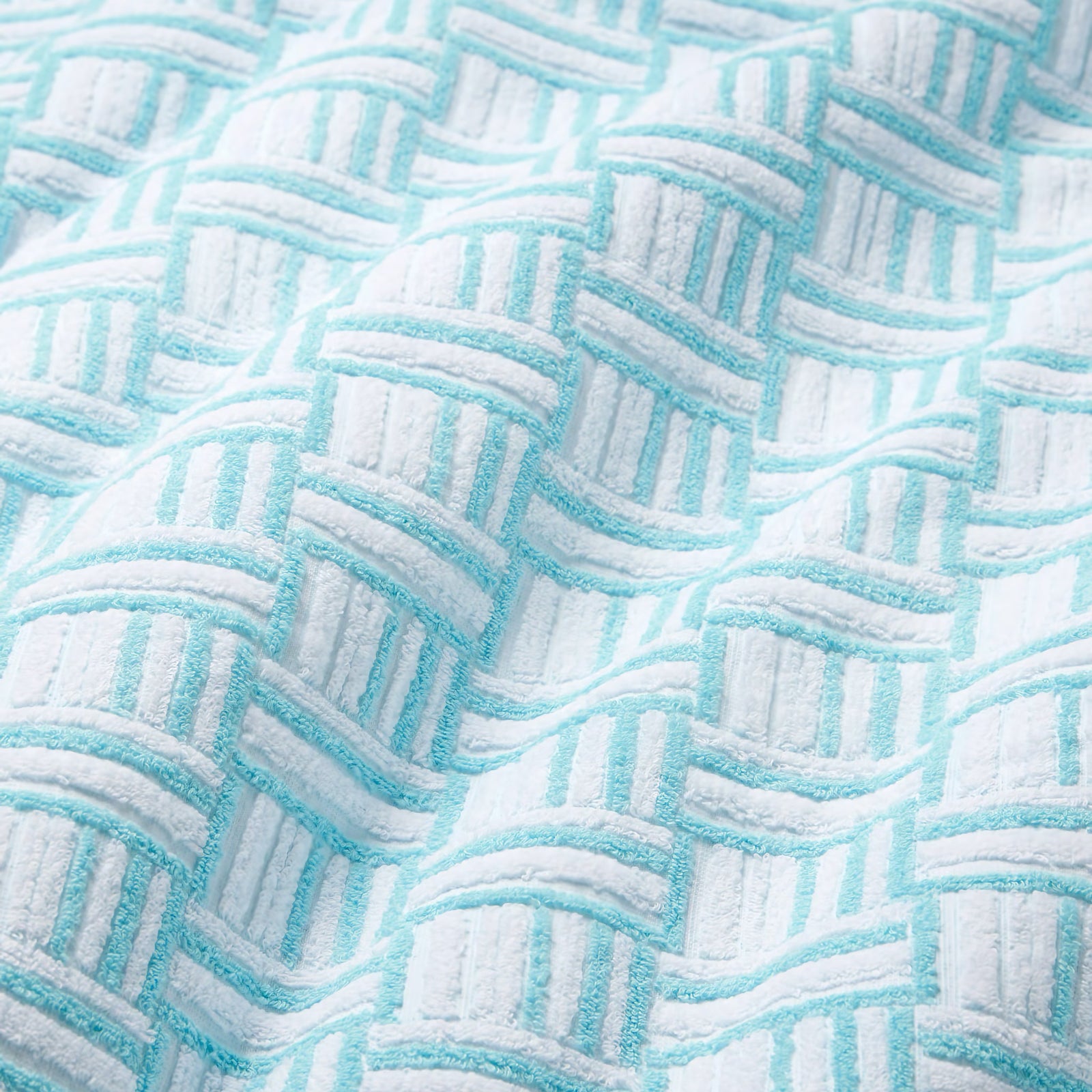 Three Sferra Tirreno Beach Towels with geometric texture hang above a woven bench, adding premium cotton comfort to your space.