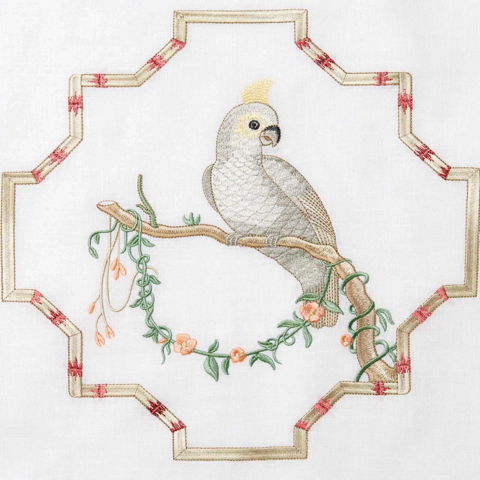 A decorative linen pillow with an embroidered bird perches on a bed with blue and patterned bedding.