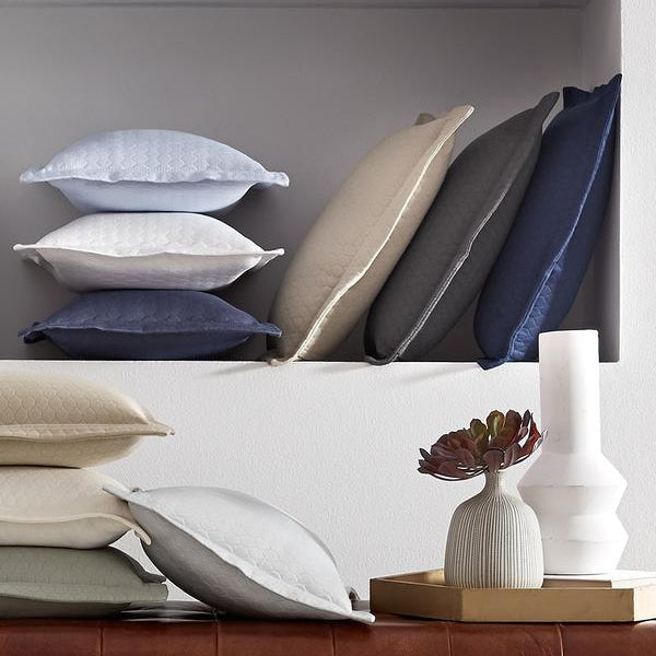 Stacked decorative pillows, including some with a honeycomb pattern, are arranged on shelves above a brown leather surface.