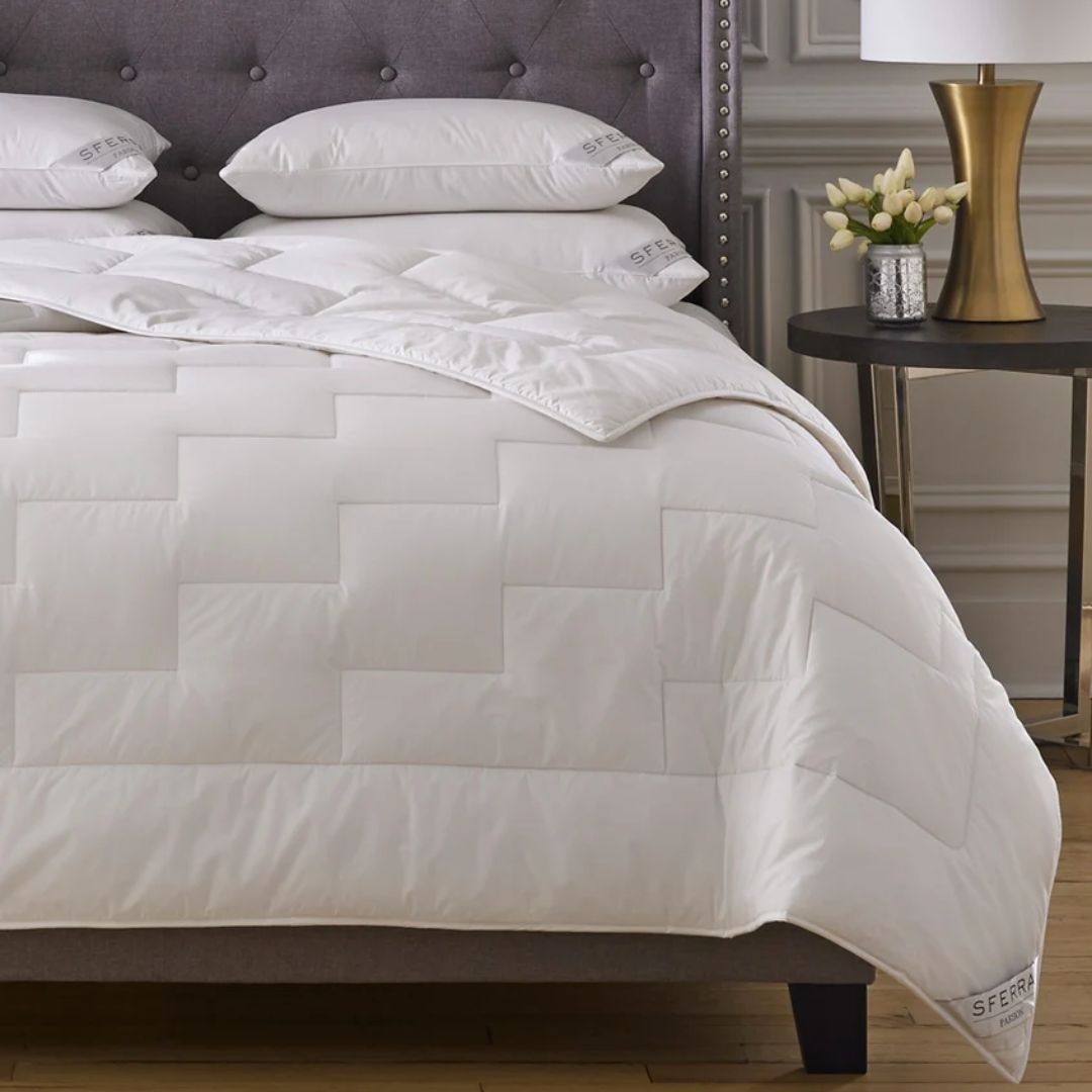White comforter on a bed with a gray headboard and side table with decor items.