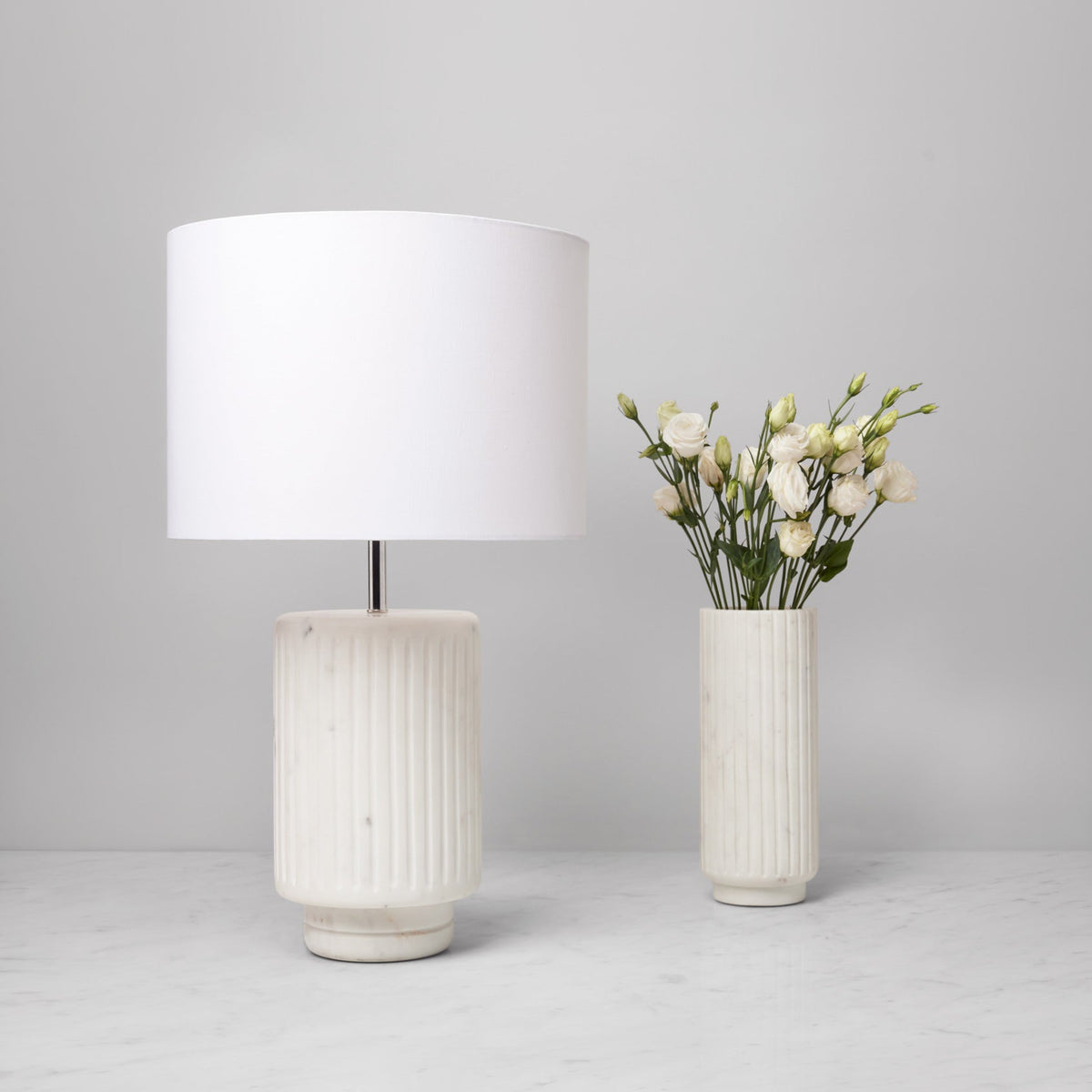 Sferra Romano vase and table lamp in white marble, vase has white flowers in it.