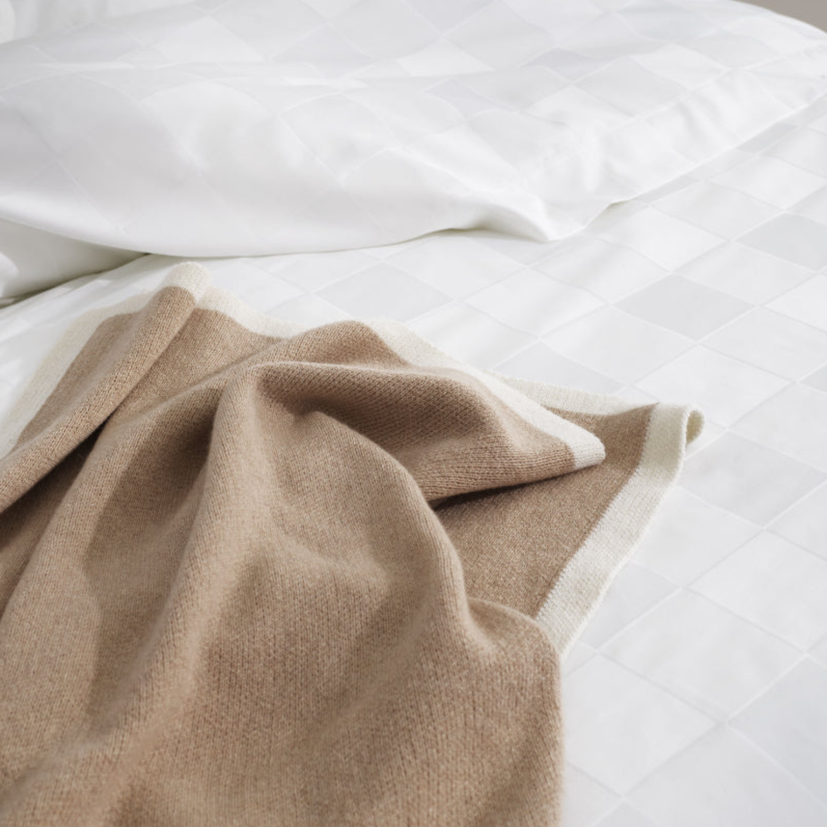 A tan jacquard weave throw blanket resting on an Amalia Sagres Giza 92 Jacquard Bedding.