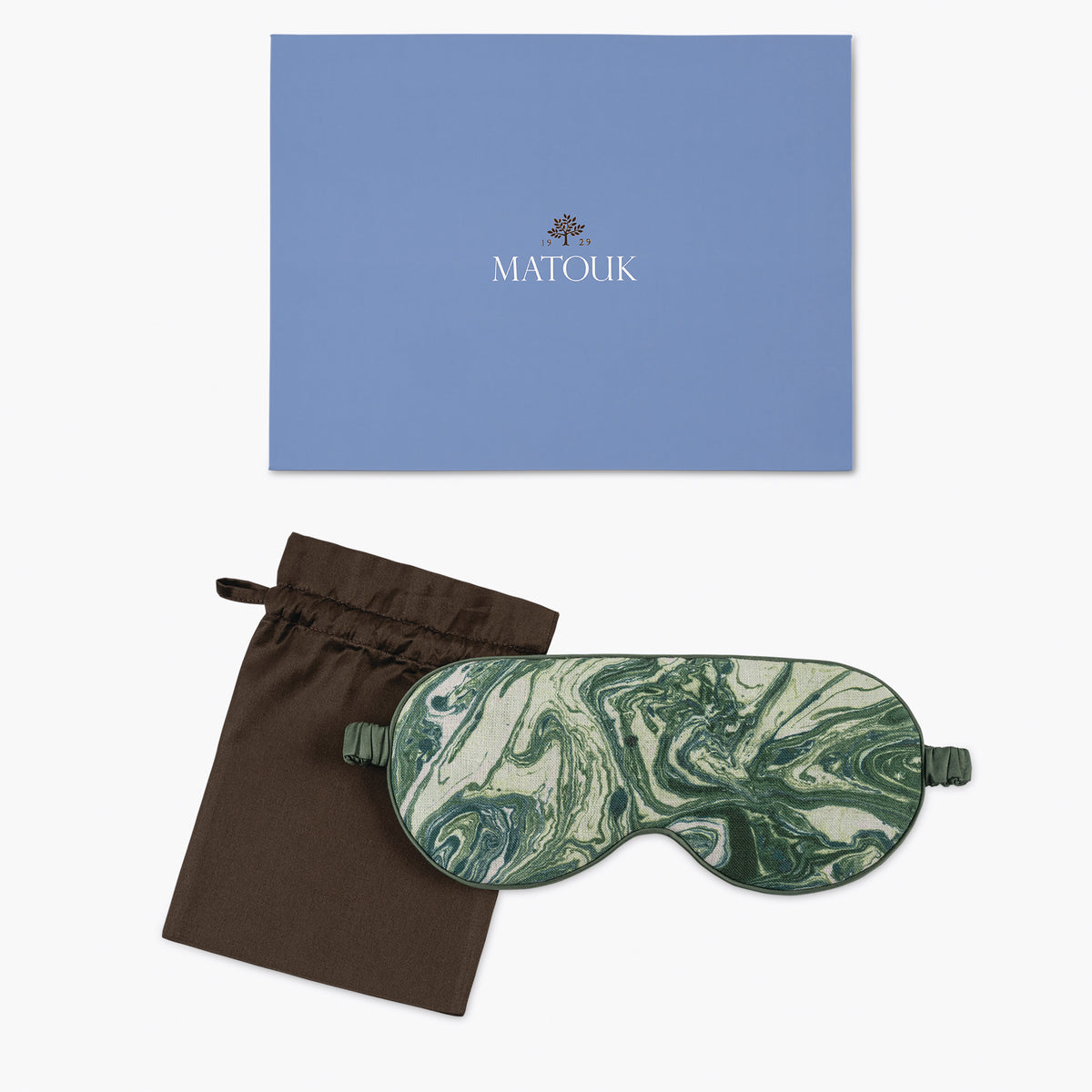 A green and white marbled linen sleep mask with a brown pouch, shown next to a blue Matouk branded box.