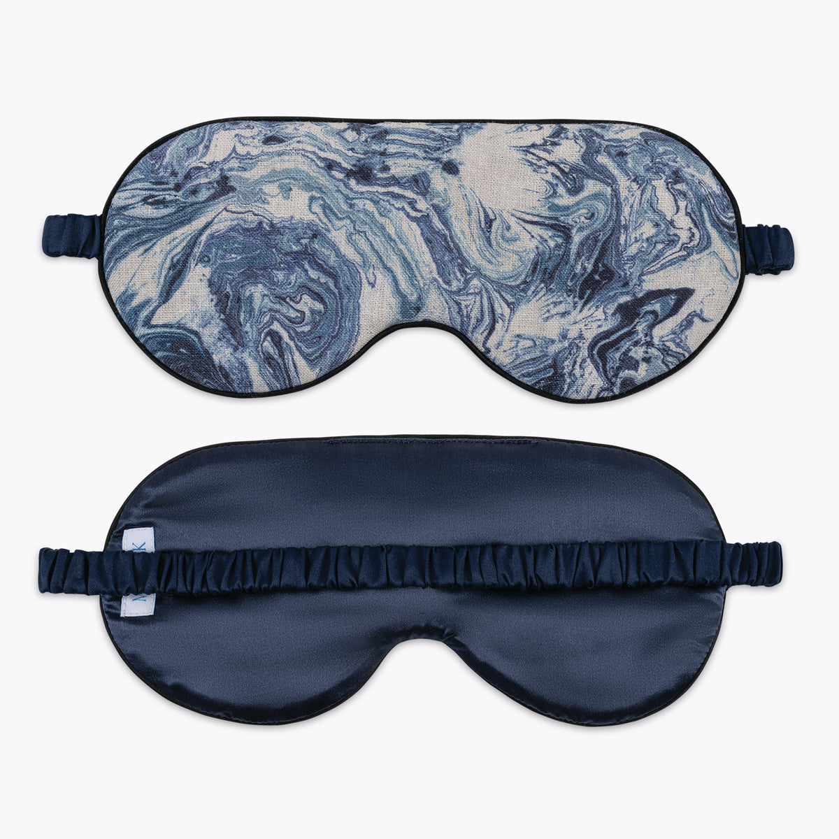 Two Matouk sleep masks, one blue marble and one navy, both with elastic straps, are laid flat on a white background.