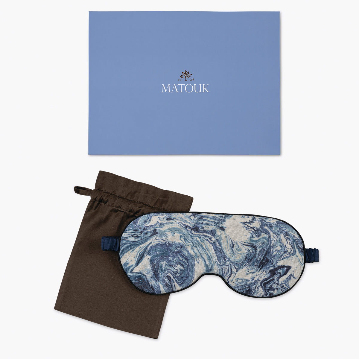A blue marbled Matouk sleep mask with a brown pouch, beside a blue box, rests on a white background.